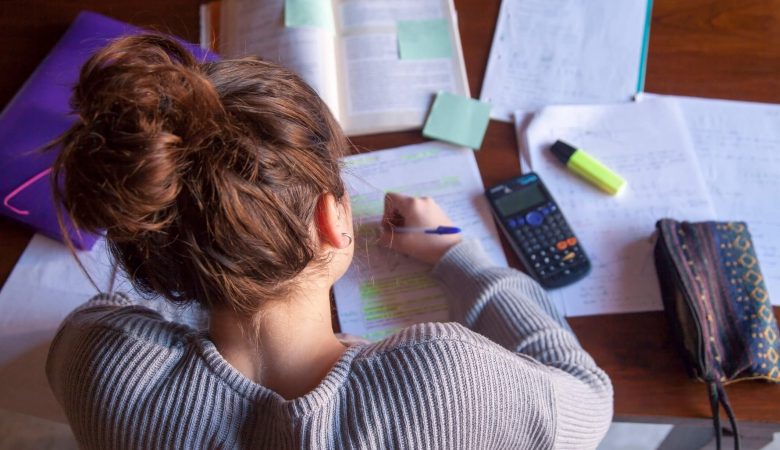 Uma menina fazendo anotações com uma caneta, cadernos, post it e calculadora em cima da mesa
