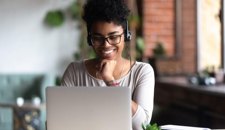 financiamento estudantil: mulher negra sorrindo ao olhar conteúdo em computador enquanto usa fones de ouvido