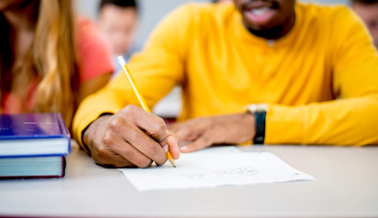 rotina de estudos: homem negro escrevendo em folha de papel A4 com caneta transparente