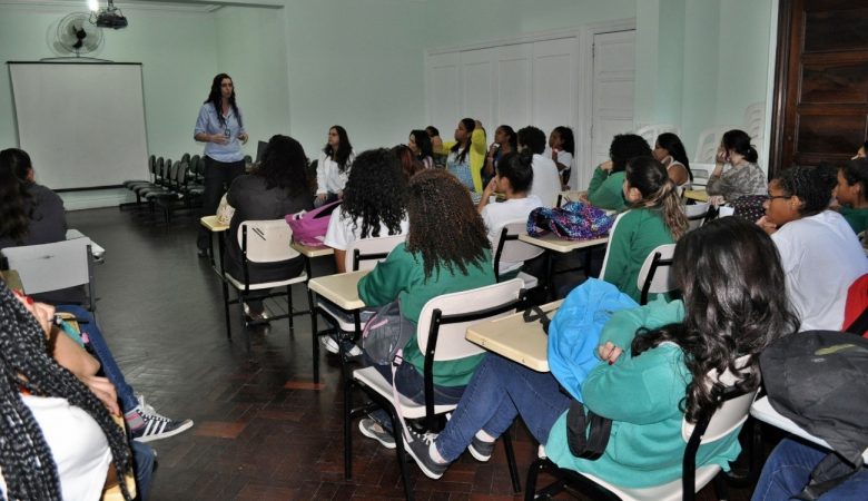 Uma sala de aula com diversos alunos e uma professora dando aula