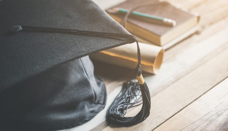 Um chapéu de formatura, um diploma e um caderno com um lápis
