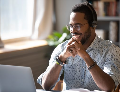Um homem com um fone de ouvido assistindo algo e sorrindo para a tela do computador