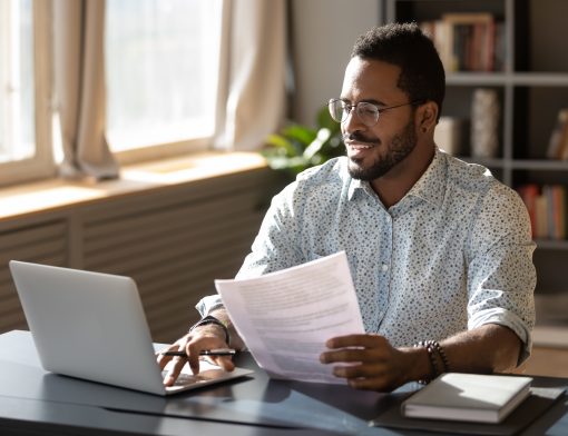 Um homem olhando para o computador e segurando um papel na mão