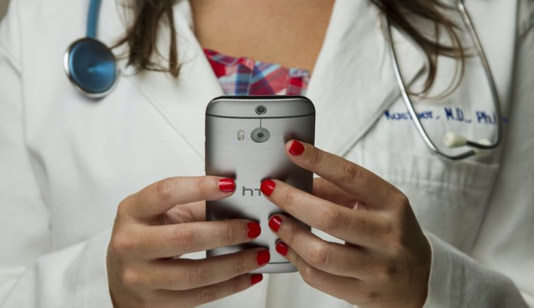 Uma mulher com roupas de médica segurando um celular nas mãos