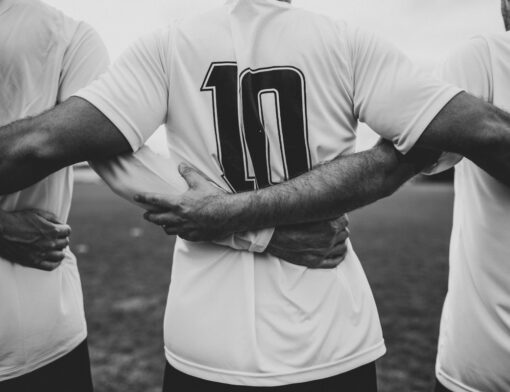 Foto em preto e branca de jogadores de futebol de costas em abraço em grupo