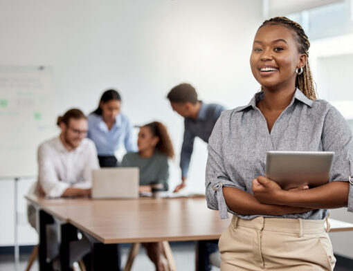 Mulher sorrindo e atrás dela um grupo de pessoas frente ao notebook