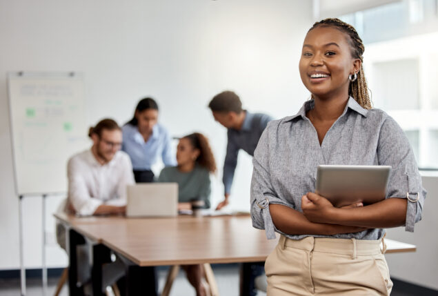 Mulher sorrindo e atrás dela um grupo de pessoas frente ao notebook